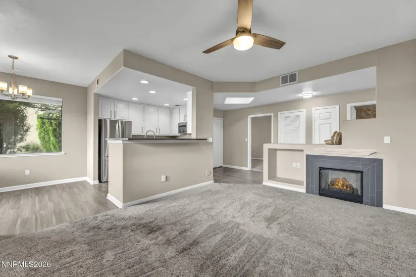 Living Room Corner View – Spacious view from the living room corner showcasing the kitchen breakfast bar, kitchen nook, fireplace, front entry, and secondary bedroom, highlighting the open and functional floor plan.