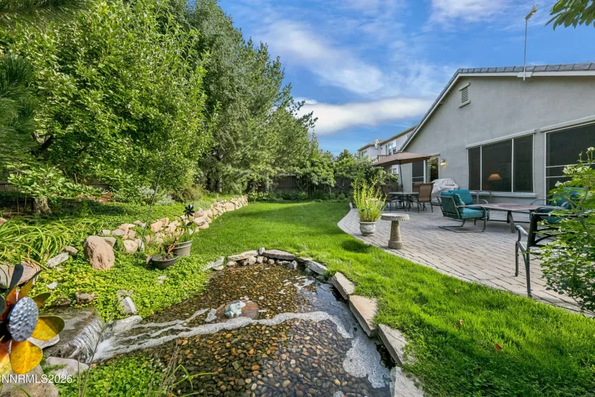 Gorgeous, lush backyard featuring a tranquil water feature and paver patio, creating a private and serene retreat ideal for outdoor entertaining and relaxation.