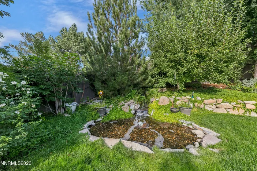 Gorgeous, lush backyard featuring a tranquil water feature and paver patio, creating a private and serene retreat ideal for outdoor entertaining and relaxation.