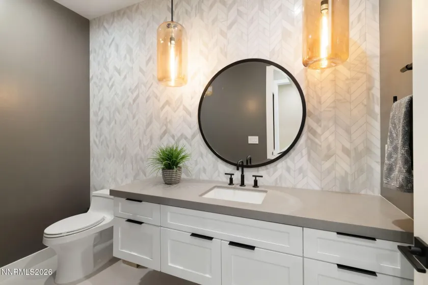 Powder bath with upgraded full wall herringbone porcelain tile backsplash. Custom pendant lighting and framed mirror